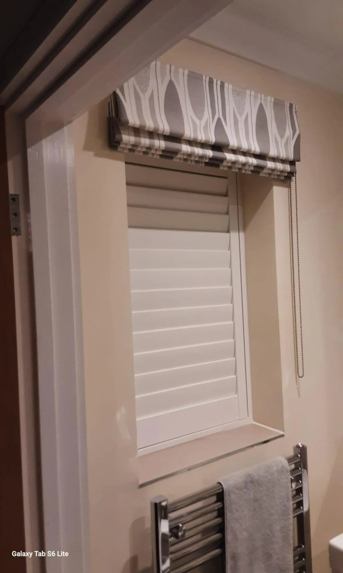Roman blind with patterned fabric above a café-style shutter in a bathroom