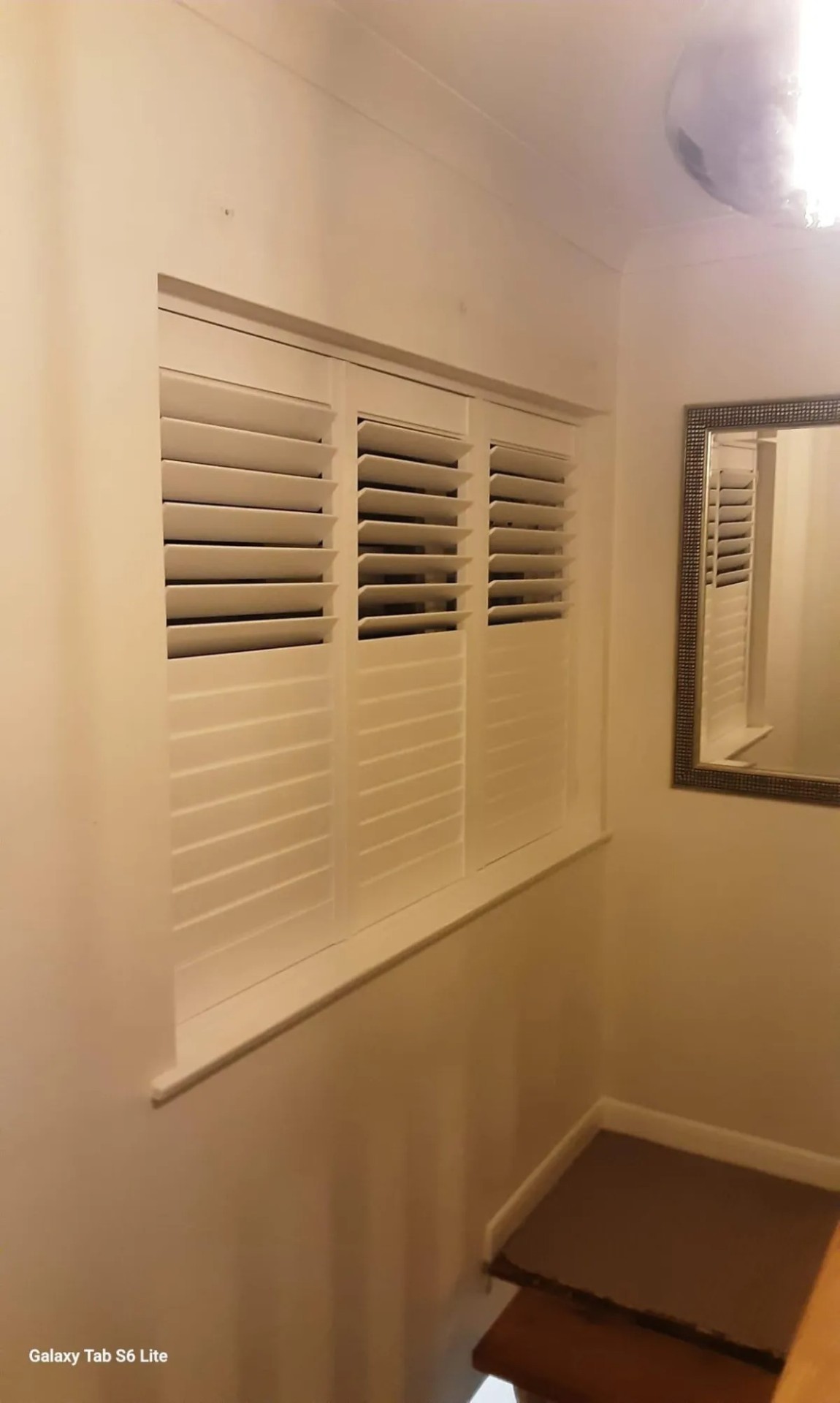 Three-panel plantation shutters fitted on a stairway landing window