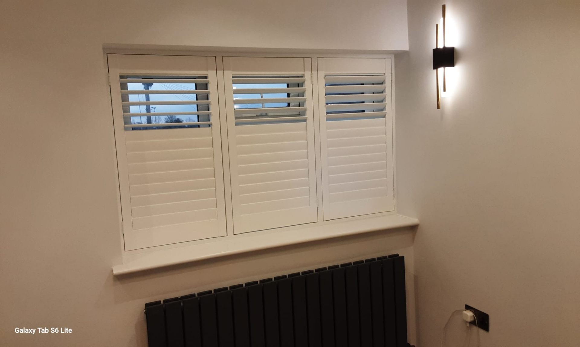 Three-panel plantation shutters with louvres tilted open above a dark radiator