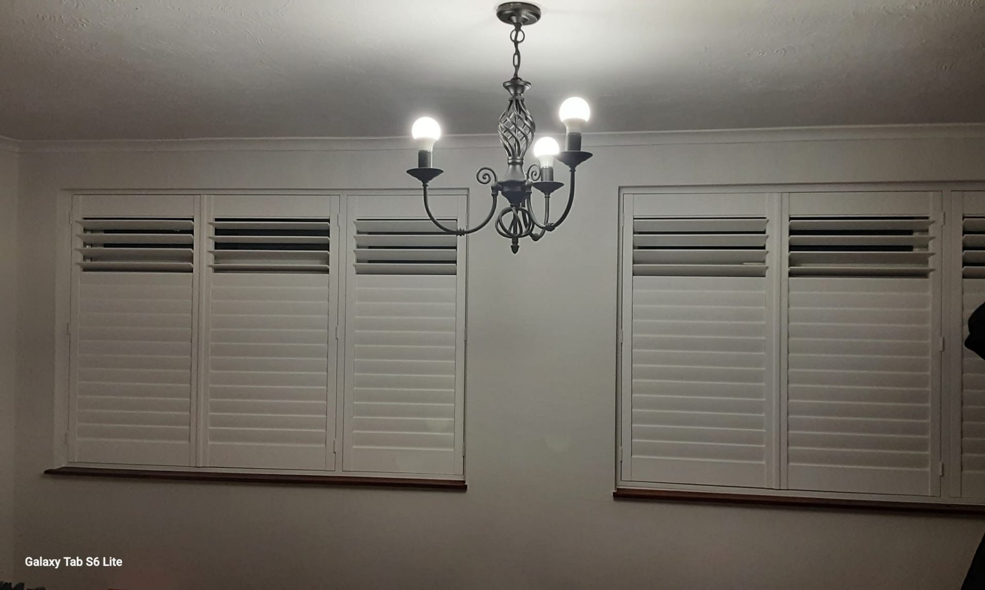 Plantation shutters closed on two windows in a room with chandelier