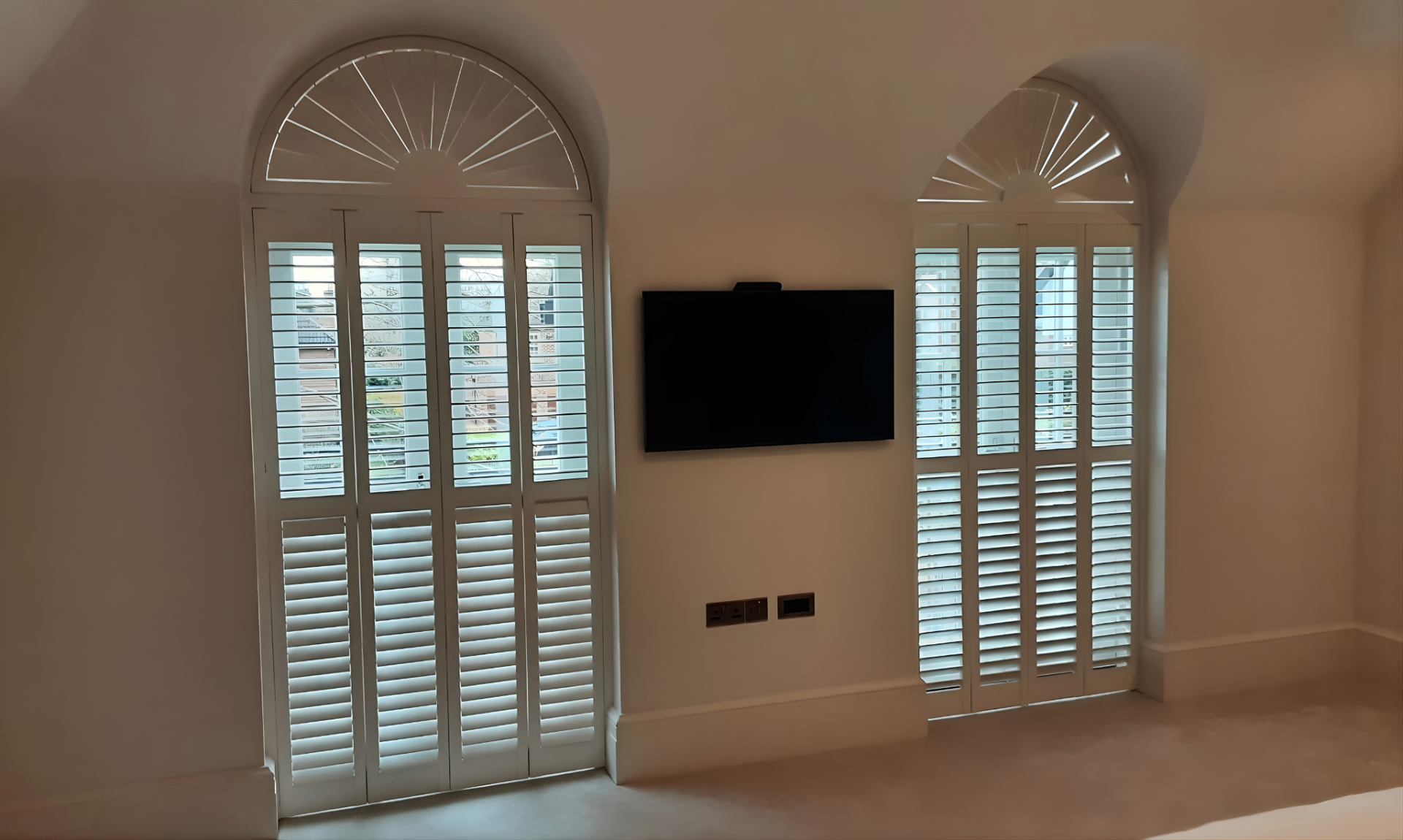 Full-height arched plantation shutters professionally installed in a living room