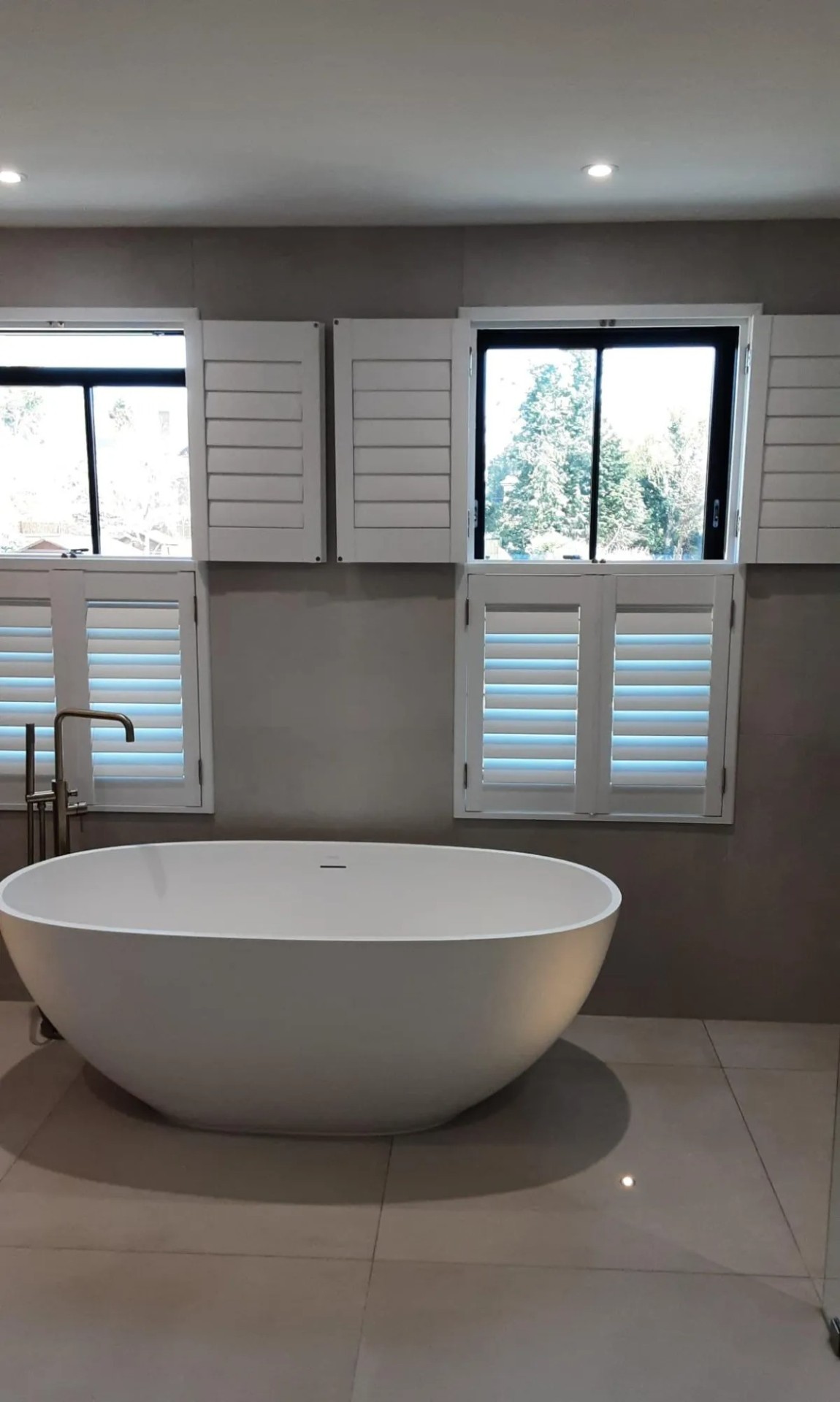 Tier-on-tier plantation shutters fitted in a modern bathroom with freestanding bathtub
